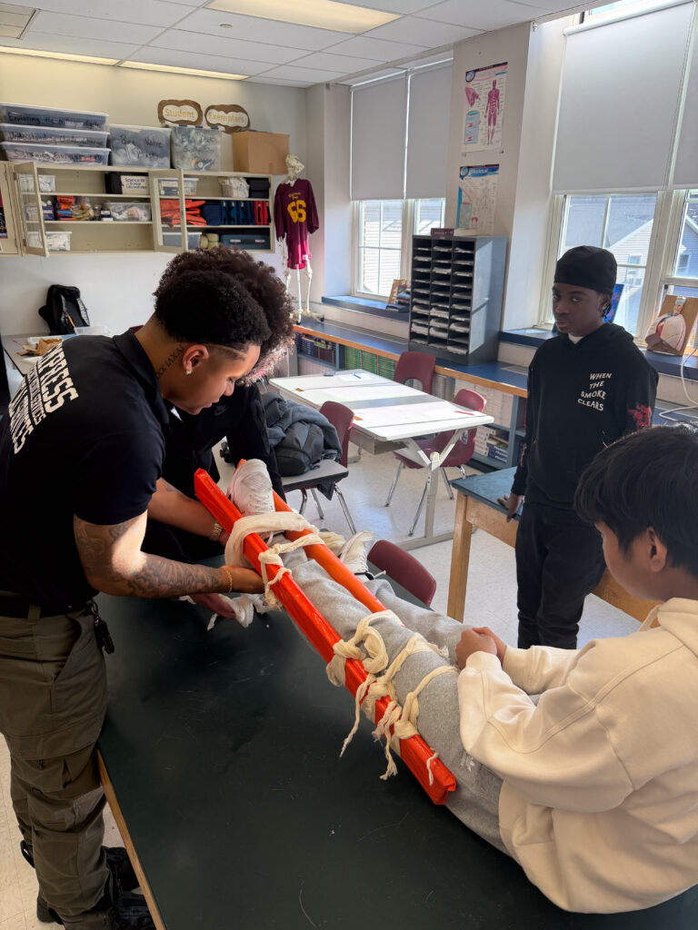 A man in uniform splints someone's leg while someone else watches.