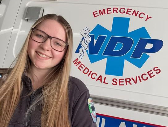A female EMT stands in front of an NDP ambulance.