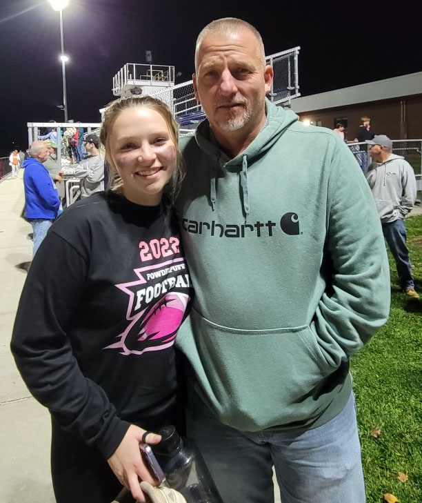 Young woman stands with Dad at game.