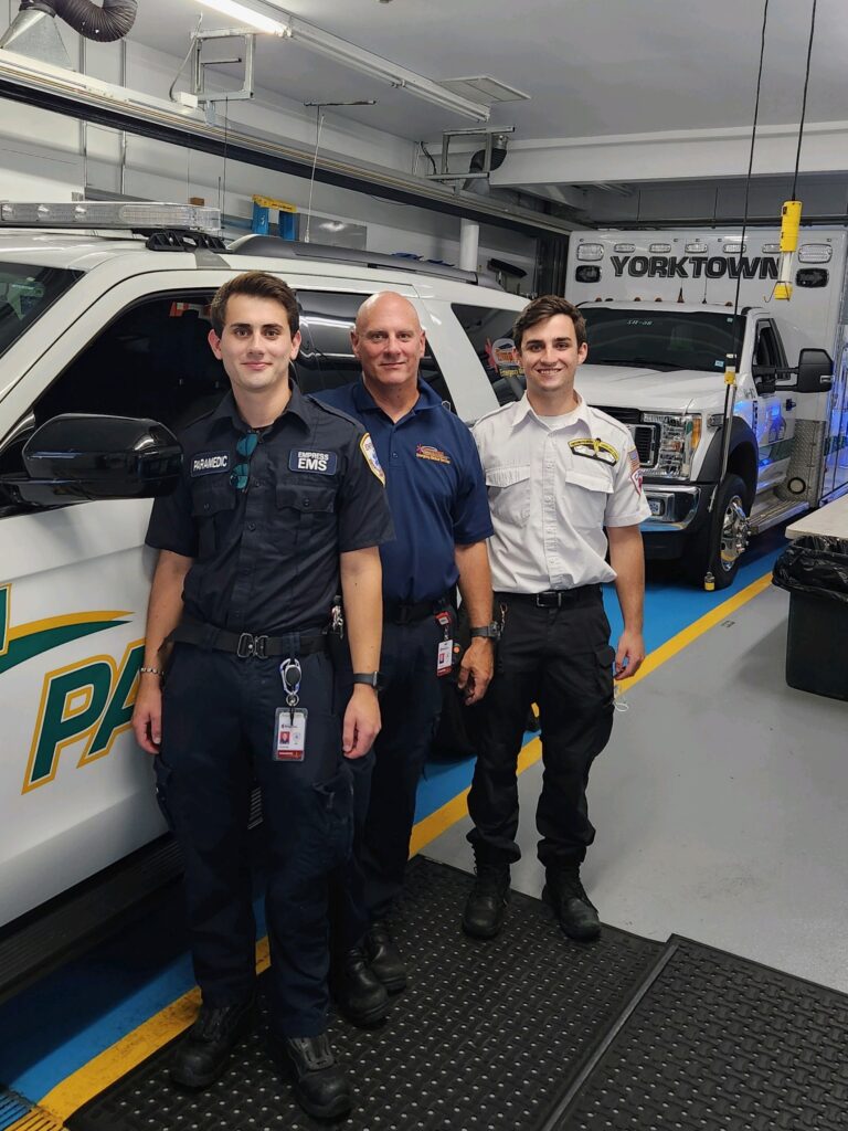 Three men pose in front of a paramedic SUV vehicle.